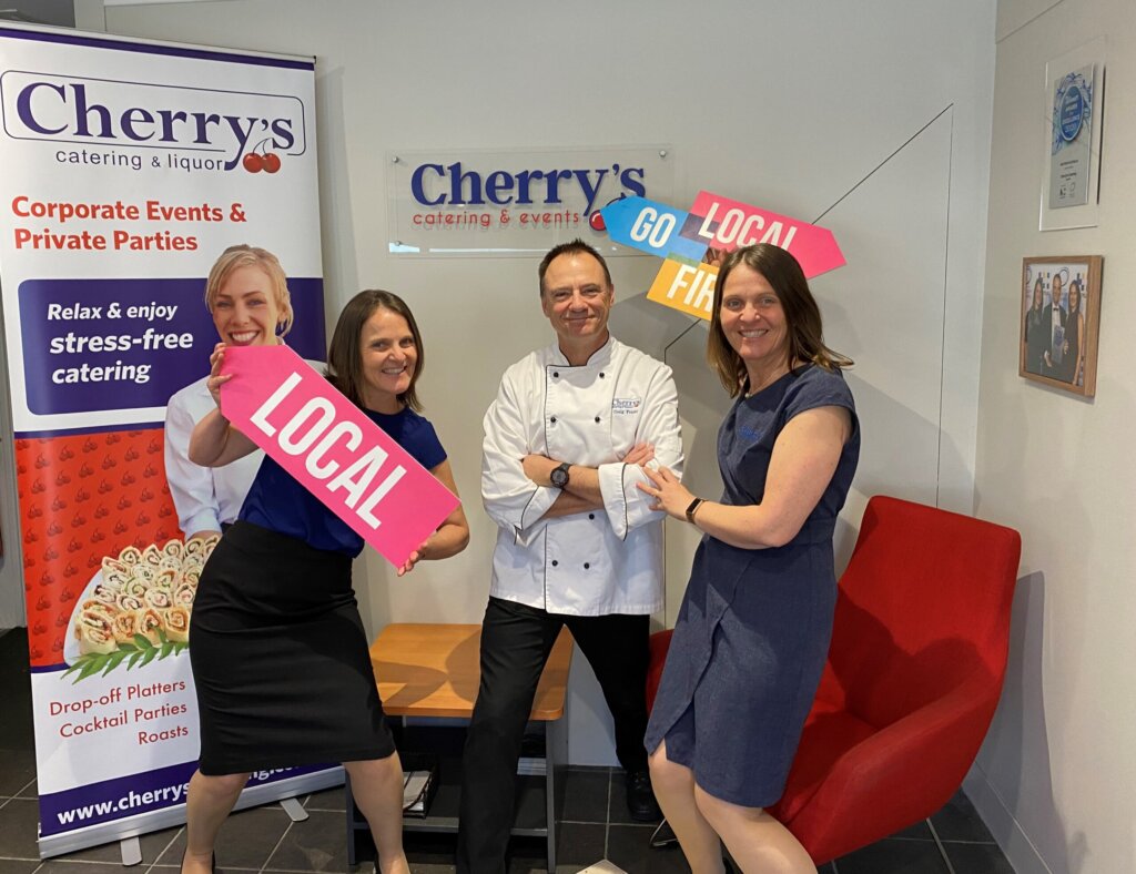 Photograph of Cherry's Catering staff and Chef holding a 'Local' sign in front of Cherry's Catering banner